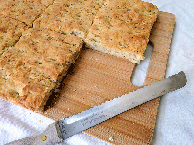 finished rosemary focaccia bread on cutting board next to bread knife