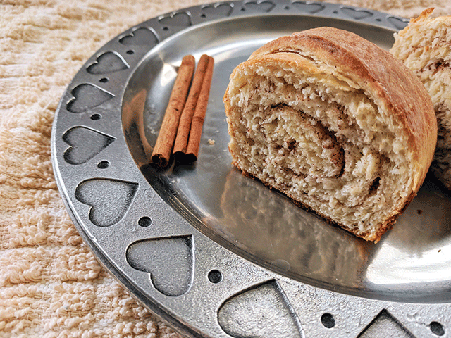 mini cinnamon swirl bread loaf on a plate next to cinnamon sticks