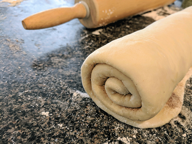 Cinnamon swirl bread dough rolled up next to rolling pin