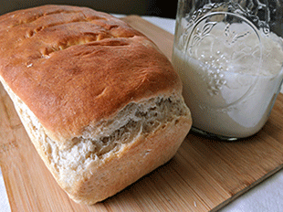sourdough bread on cutting board with sourdough starter
