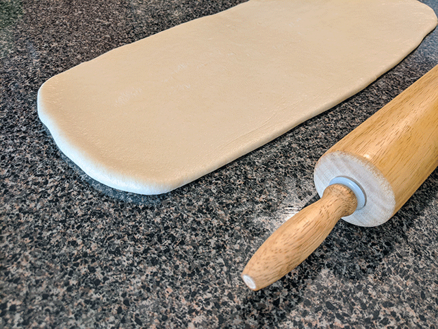 flattened cinnamon raisin sourdough bread dough next to rolling pin