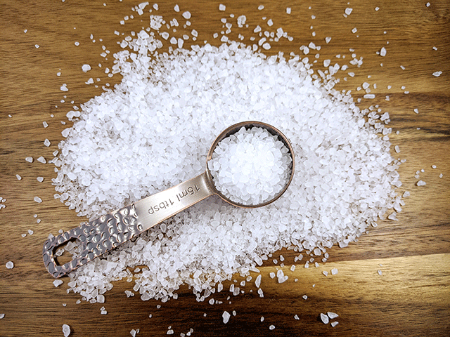 spoon full of salt on wood cutting board with more salt