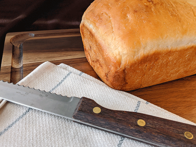 uncut cinnamon swirl raisin sourdough discard bread on a cutting board with bread knife and tea towel