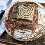 loaf of pain de campagne bread on cutting board with knife and tea towel