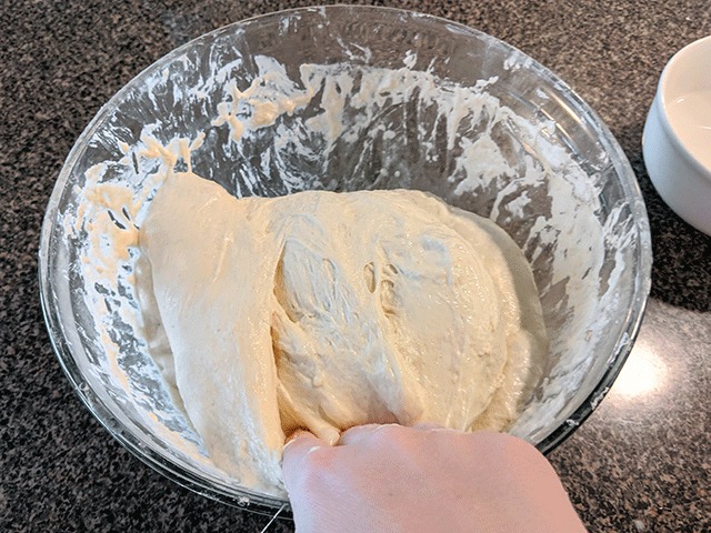 folding bread dough in a glass bowl
