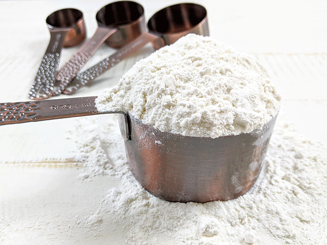 measuring cups with flour on wooden table
