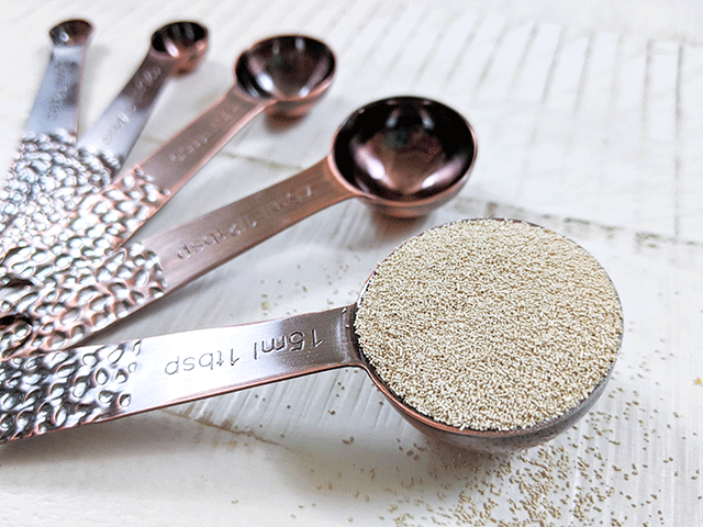measuring spoons filled with yeast on wooden table
