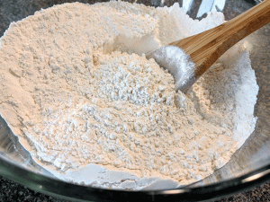 flour in a glass bowl with a wooden mixing spoon