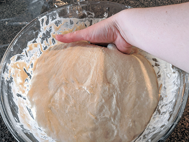hand scooping dough in a glass bowl