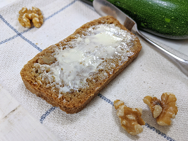 buttered slice of zucchini walnut bread next to walnuts and zucchini