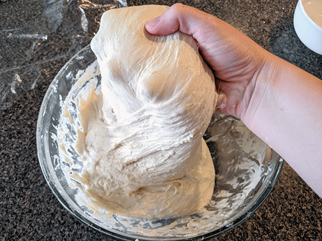 hand stretching dough over a glass bowl