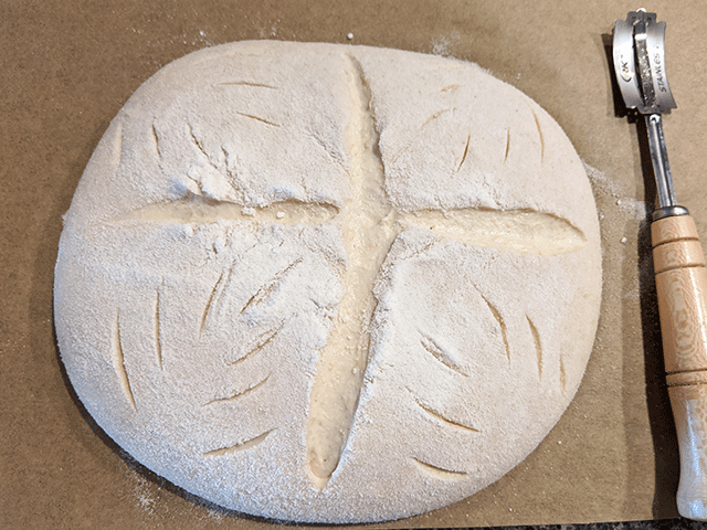 dough scored on parchment paper next to bread lame