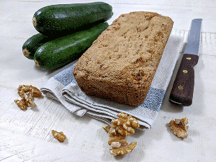 zucchini walnut bread on tea towel next to bread knife and zucchini and walnuts