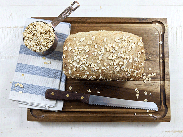maple oat sourdough sandwich bread on cutting board with knife and cup of oats